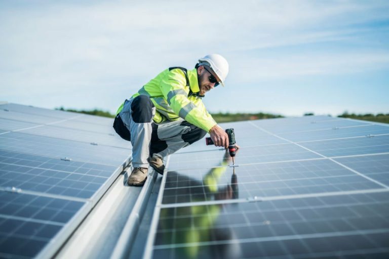 Male worker on a roof using drill to fix solar panel.