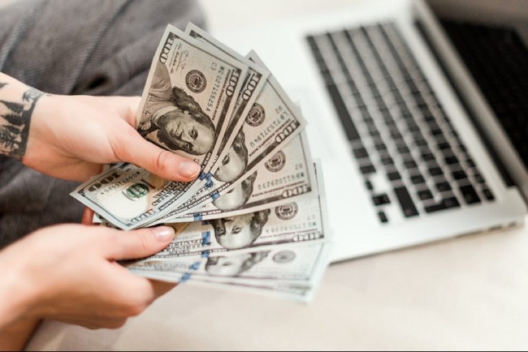 1600951323-close-up-woman-hands-holding-new-dollar-bills-she-earned-working-from-laptop-home-online-97712-81 (1)